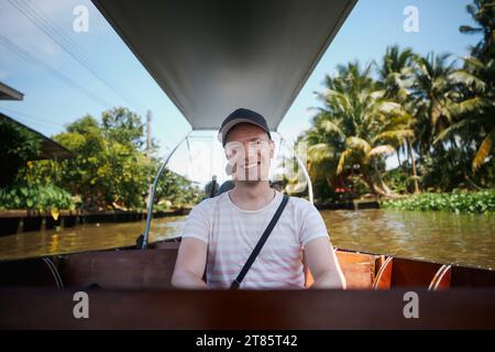 Porträt eines lächelnden Touristen auf dem Boot. Man genießt Urlaub auf einem Bootsausflug zum schwimmenden Markt Damnoen Saduak in Ratchaburi in der Nähe von Bangkok, Thailand. Stockfoto
