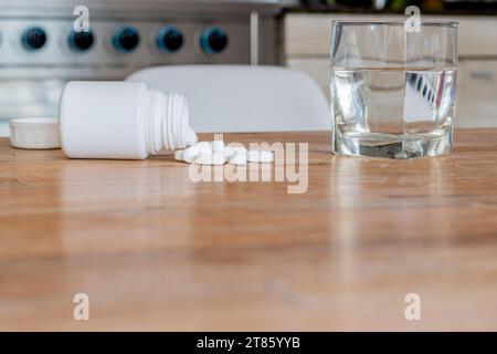 Pillen mit einem Glas Wasser auf dem Küchentisch. Stockfoto