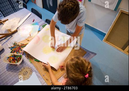 Draufsicht auf Kinder, die Bleistifte halten und auf weißem Papier zeichnen, in einer Kreativkunstwerkstatt. Kreativität und künstlerisches Kompetenzentwicklungskonzept. Kinder A Stockfoto