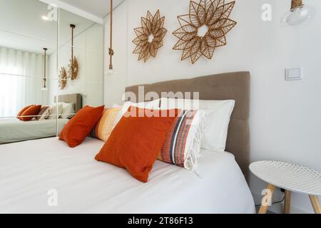 Doppelbett im hellen Schlafzimmer Innenmöbel. Rote dekorative Kissen und Lampenschirme im Vordergrund. Stockfoto