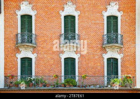 Backsteinmauer mit sechs dunkelgrünen Balkontüren, die zum schmalen Balkon in Bellagio führen Stockfoto