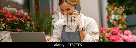 Ein lächelnder Blumenhändler, der einen Laptop aussah, bekam Bestellung an der Theke ihres Blumenladens Stockfoto