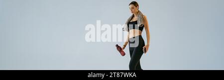 Eine Frau, die mit einer Wasserflasche und einem Handtuch um den Hals läuft, über den Studiohintergrund Stockfoto