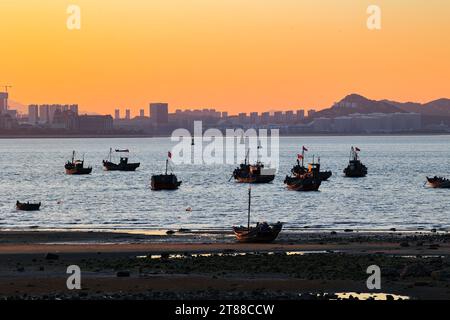 QINGDAO, CHINA - 18. NOVEMBER 2023 - Fischerboote segeln bei Sonnenuntergang an der Küste der Insel Gujia im New Areal der Westküste von Qingdao, Shandong Prov Stockfoto