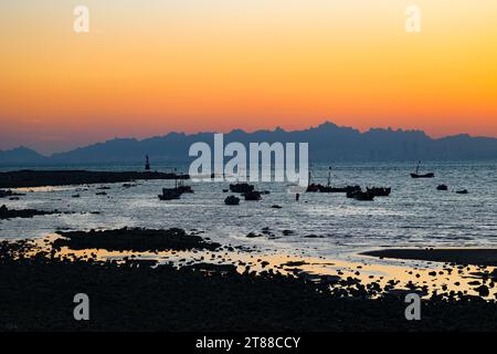 QINGDAO, CHINA - 18. NOVEMBER 2023 - Fischerboote segeln bei Sonnenuntergang an der Küste der Insel Gujia im New Areal der Westküste von Qingdao, Shandong Prov Stockfoto