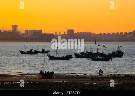 QINGDAO, CHINA - 18. NOVEMBER 2023 - Fischerboote segeln bei Sonnenuntergang an der Küste der Insel Gujia im New Areal der Westküste von Qingdao, Shandong Prov Stockfoto