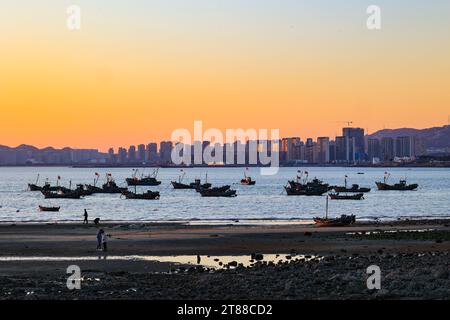 QINGDAO, CHINA - 18. NOVEMBER 2023 - Fischerboote segeln bei Sonnenuntergang an der Küste der Insel Gujia im New Areal der Westküste von Qingdao, Shandong Prov Stockfoto