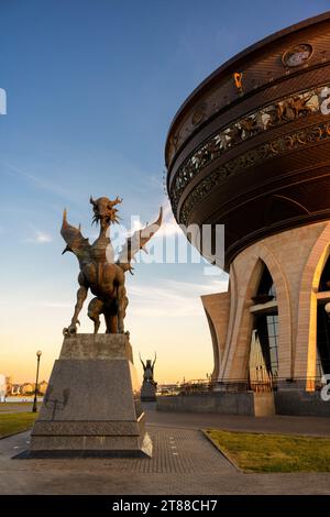 Hochzeitspalast und Drachenstatue bei Sonnenuntergang in Kasan, Tatarstan, Russland. Vertikaler Blick auf riesige Schüssel, Himmel und moderne Skulpturen, Wahrzeichen der Stadt. Design Stockfoto