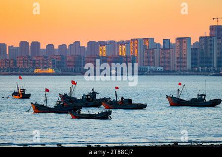 QINGDAO, CHINA - 18. NOVEMBER 2023 - Fischerboote segeln bei Sonnenuntergang an der Küste der Insel Gujia im New Areal der Westküste von Qingdao, Shandong Prov Stockfoto