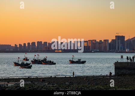 QINGDAO, CHINA - 18. NOVEMBER 2023 - Fischerboote segeln bei Sonnenuntergang an der Küste der Insel Gujia im New Areal der Westküste von Qingdao, Shandong Prov Stockfoto