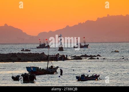 QINGDAO, CHINA - 18. NOVEMBER 2023 - Fischerboote segeln bei Sonnenuntergang an der Küste der Insel Gujia im New Areal der Westküste von Qingdao, Shandong Prov Stockfoto