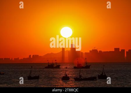QINGDAO, CHINA - 18. NOVEMBER 2023 - Fischerboote segeln bei Sonnenuntergang an der Küste der Insel Gujia im New Areal der Westküste von Qingdao, Shandong Prov Stockfoto