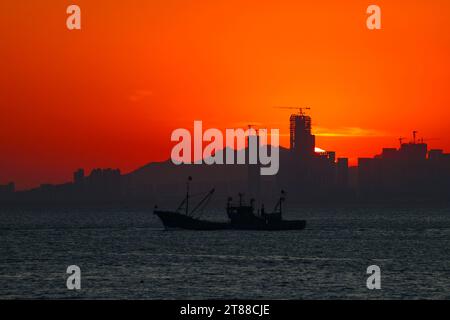 QINGDAO, CHINA - 18. NOVEMBER 2023 - Fischerboote segeln bei Sonnenuntergang an der Küste der Insel Gujia im New Areal der Westküste von Qingdao, Shandong Prov Stockfoto