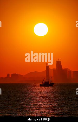 QINGDAO, CHINA - 18. NOVEMBER 2023 - Fischerboote segeln bei Sonnenuntergang an der Küste der Insel Gujia im New Areal der Westküste von Qingdao, Shandong Prov Stockfoto