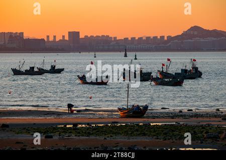 QINGDAO, CHINA - 18. NOVEMBER 2023 - Fischerboote segeln bei Sonnenuntergang an der Küste der Insel Gujia im New Areal der Westküste von Qingdao, Shandong Prov Stockfoto
