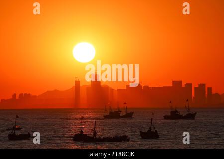 QINGDAO, CHINA - 18. NOVEMBER 2023 - Fischerboote segeln bei Sonnenuntergang an der Küste der Insel Gujia im New Areal der Westküste von Qingdao, Shandong Prov Stockfoto