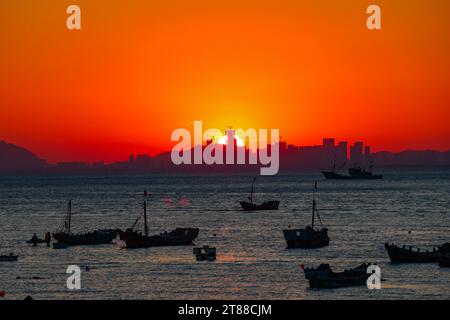 QINGDAO, CHINA - 18. NOVEMBER 2023 - Fischerboote segeln bei Sonnenuntergang an der Küste der Insel Gujia im New Areal der Westküste von Qingdao, Shandong Prov Stockfoto