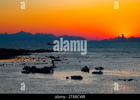 QINGDAO, CHINA - 18. NOVEMBER 2023 - Fischerboote segeln bei Sonnenuntergang an der Küste der Insel Gujia im New Areal der Westküste von Qingdao, Shandong Prov Stockfoto