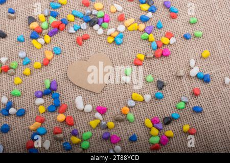 Herz aus Papier inmitten der bunten Steinchen auf Leinwand Boden Stockfoto