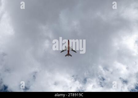 Ein Passagierflugzeug fliegt direkt über dem Himmel, umrissen vor einem bewölkten Himmel und viel leerem Raum. Stockfoto