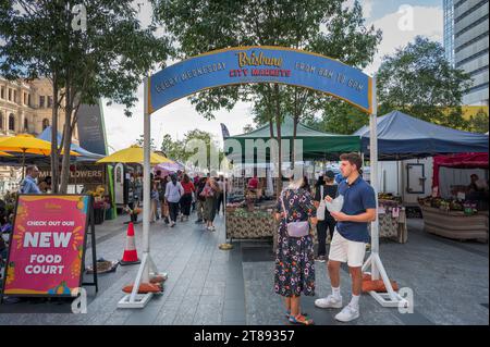 Ein junges Paar steht in der Nähe des Bogenschilds der Brisbane City Markets und probiert einige der Speisen, die Einheimischen und Touristen gleichermaßen zur Verfügung stehen. Stockfoto