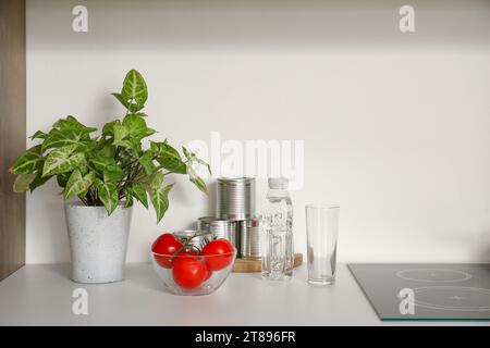 Zimmerpflanze, Schüssel mit Tomaten und Flasche Wasser auf weißer Küchenzeile Stockfoto