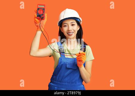 Junge Elektrikerin mit Multimeter und Drähten auf orangem Hintergrund Stockfoto