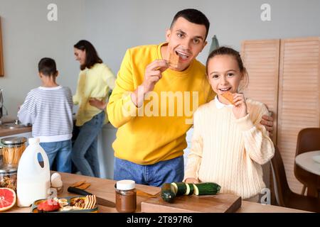 Ein kleines Mädchen mit ihrem Vater isst Cracker in der Küche Stockfoto