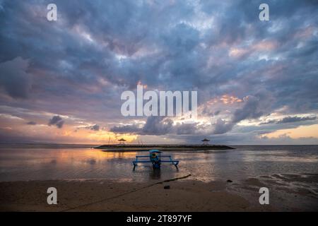 Sonnenaufgang am Sandstrand von Sanur. Tempel im Wasser. Traditionelles Fischerboot, Jukung am Strand. Hinduglaub in Sanur auf Bali. Trauminsel Stockfoto