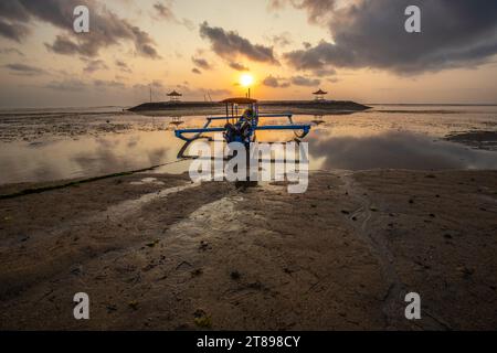 Sonnenaufgang am Sandstrand von Sanur. Tempel im Wasser. Traditionelles Fischerboot, Jukung am Strand. Hinduglaub in Sanur auf Bali. Trauminsel Stockfoto