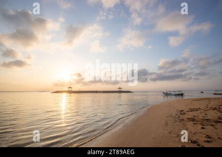 Sonnenaufgang am Sandstrand von Sanur. Tempel im Wasser. Traditionelles Fischerboot, Jukung am Strand. Hinduglaub in Sanur auf Bali. Trauminsel Stockfoto