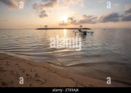 Sonnenaufgang am Sandstrand von Sanur. Tempel im Wasser. Traditionelles Fischerboot, Jukung am Strand. Hinduglaub in Sanur auf Bali. Trauminsel Stockfoto