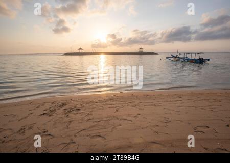 Sonnenaufgang am Sandstrand von Sanur. Tempel im Wasser. Traditionelles Fischerboot, Jukung am Strand. Hinduglaub in Sanur auf Bali. Trauminsel Stockfoto