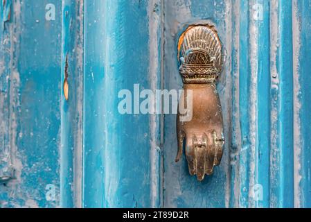 Hintergrund einer alten blauen Holztür mit einem bronzenen Griff in Handform. Stockfoto