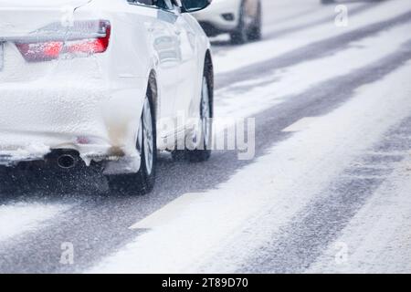 Weiße, schneebedeckte Autos fahren am Wintertag auf einer schneebedeckten Straße Stockfoto