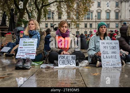 London, Großbritannien. November 2023. Die Demonstranten halten Plakate, während sie bei regnerischem Wetter auf dem Parlamentsplatz auf dem Boden sitzen. Die Mütter-Rebellion organisierte eine kleine Protestveranstaltung auf dem Parliament Square in London, Großbritannien. Quelle: SOPA Images Limited/Alamy Live News Stockfoto