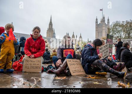 London, Großbritannien. November 2023. Die Demonstranten halten Plakate, während sie bei regnerischem Wetter auf dem Parlamentsplatz auf dem Boden sitzen. Die Mütter-Rebellion organisierte eine kleine Protestveranstaltung auf dem Parliament Square in London, Großbritannien. Quelle: SOPA Images Limited/Alamy Live News Stockfoto