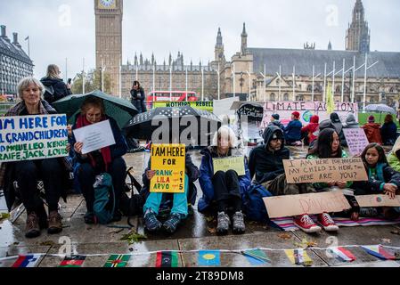 London, Großbritannien. November 2023. Die Demonstranten halten ein Plakat, während sie bei regnerischem Wetter auf dem Parlamentsplatz auf dem Boden sitzen. Die Mütter-Rebellion organisierte eine kleine Protestveranstaltung auf dem Parliament Square in London, Großbritannien. Quelle: SOPA Images Limited/Alamy Live News Stockfoto