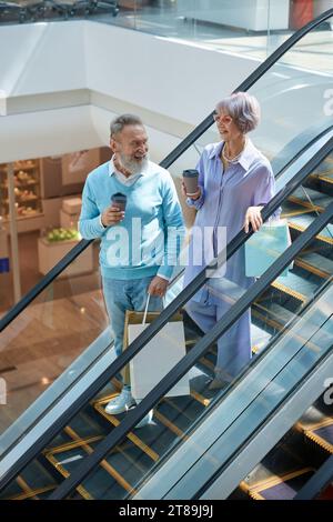 Seniorenpaar, das die Rolltreppe des Einkaufszentrums herunterfährt und die Zeit zusammen genießt Stockfoto