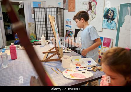 Talentierte Kinder im Grundalter, selbstbewusste Jugendliche Jungen und Mädchen, inspirierte Künstler, die an der Staffelei stehen und Aquarelle bemalen Stockfoto