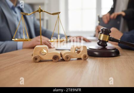 Kleine Holzspielzeugautos vor dem Hammer und der Waage des Richters. Autounfall, Kfz-Versicherungskonzept. Stockfoto