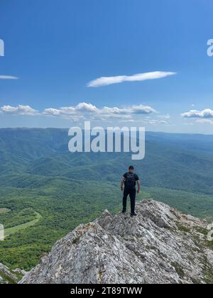 Ein Mann steht auf einem Berg und schaut in die Ferne unter einem blauen Himmel Wanderweg Stockfoto