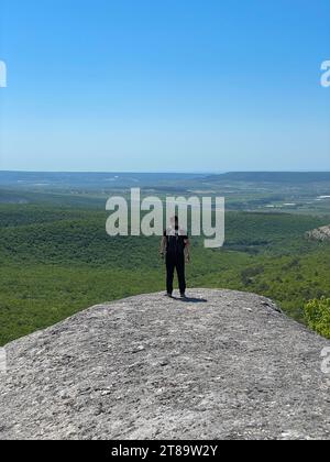 Ein Mann steht auf einem Berg und schaut in die Ferne unter einem blauen Himmel Wanderweg Stockfoto