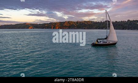 Binic, Bretagne, Frankreich - 18. August 2023: Ein kleines Segelboot, das in den Hafen von Binic einfährt und bei Sonnenuntergang mit goldenen Lichtern an der Küste gefahren wird Stockfoto