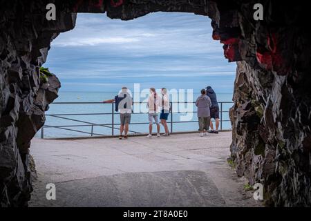 Binic, Bretagne, Frankreich - 18. August 2023: Foto von einer in den Felsen gegrabenen Passage von fünf Touristen, die von einem Kai aus auf das Meer schauen, aufgenommen in einem Stockfoto