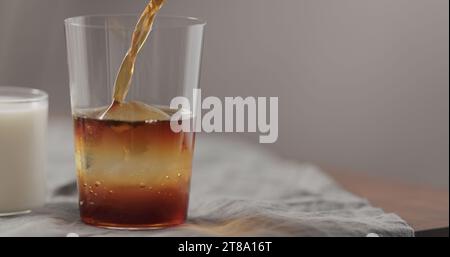 Gießen Sie kalten Brühkaffee in Glas auf Walnusstisch, breites Foto Stockfoto