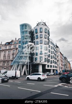 Vertikales Foto des Tanzhauses in Prag (Tschechische Republik) mit Verkehr auf der Kreuzung im Vordergrund und dramatisch bewölktem Himmel im Hintergrund. Architektur Stockfoto