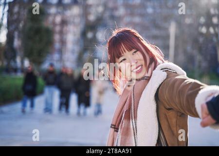 Eine junge asiatische Frau, die den Arm eines Mannes auf einer Stadtstraße zieht Stockfoto