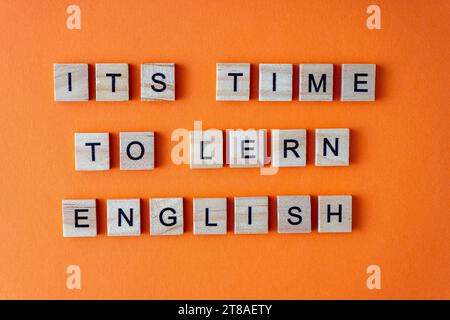 Es ist Zeit, Englisch zu lernen. Motivation. Der Satz ist in Holzbuchstaben von oben angeordnet. Motivation. Orangefarbener flacher Lay-Hintergrund Stockfoto