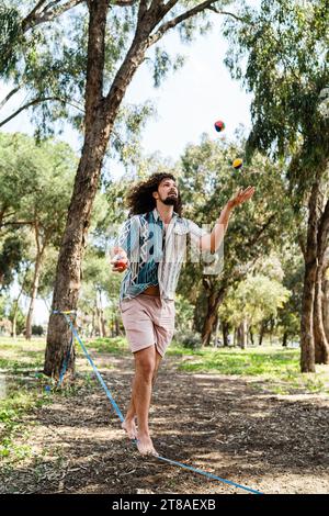 Selbstbewusster junger Mann, der auf der Slackline im Stadtpark jongliert und balanciert Stockfoto